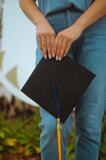 Two hands are shown holding a graduation cap